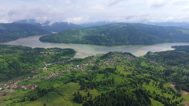 Stunning aerial footage flying over the vast Lake Bicaz in Romania. Green hills, lush forests, and picturesque villages dot the landscape