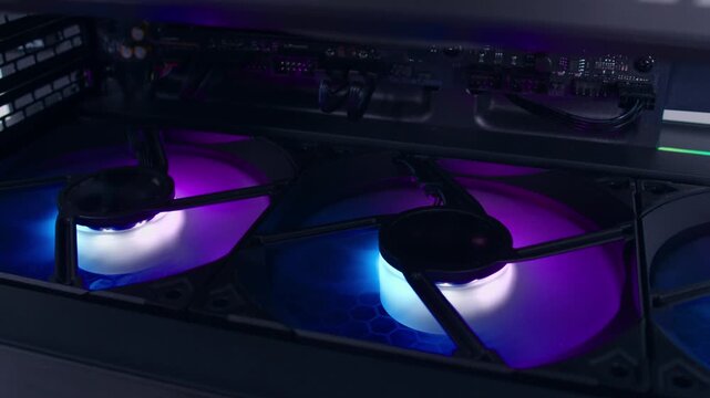 Extreme close-up of the colorful fans spinning on the computer's case illuminated by colorful LED lights
