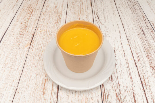 "Smooth Pumpkin Cream Soup Served Plain in Kraft Paper Cup on White Plate"