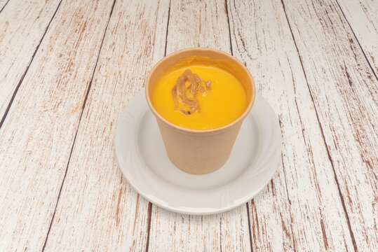 "Creamy Carrot Soup Garnished with Caramelized Onions Served in Kraft Paper Cup"