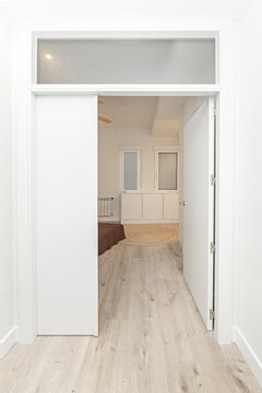 White sliding and hinged doors with a frosted transom window leading to a bedroom with light wood floors.