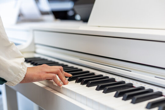 Close-Up of a Hand Playing a White Digital Piano. A persons hand plays the black and white keys of a white digital piano in a bright indoor setting with shallow focus.