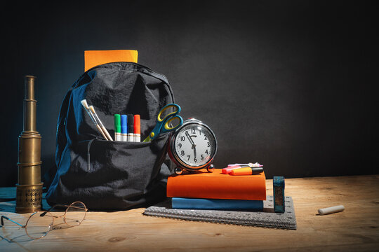 Backpack full of school supplies on table, isolated on free blackboard background.
