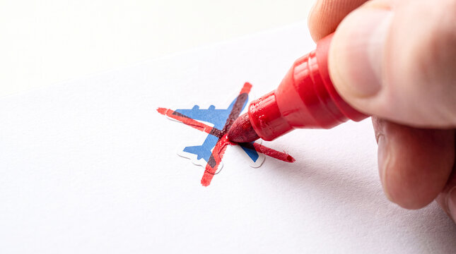 Hand drawing red X mark on paper. Person crossing out a blue airplane icon with marker.