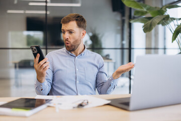 Fototapeta premium Man reacting with shock and confusion to disease news on smartphone, receiving unexpected health alert at office desk