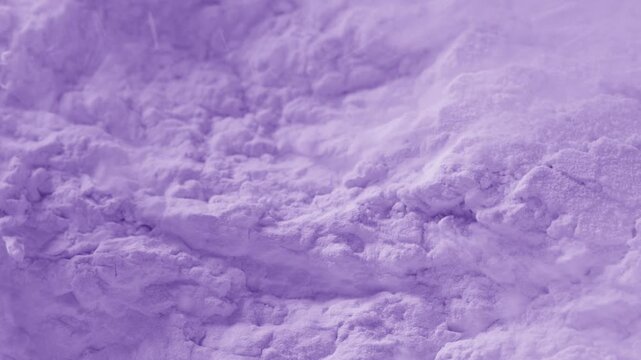 Slow-motion close-up macro shot of severed violet powder surface being blown with a strong air stream, breaking its structure and chipping it into small pieces