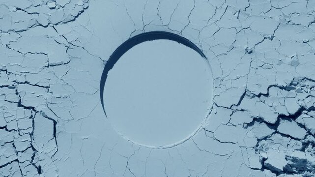 From-above shot of a pale blue flattened powder surface with cracks and a round imprint illuminated by orbiting directional light creating shadow movement