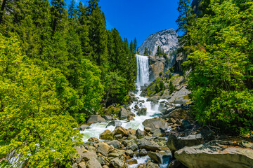Wide landscape shot of Vernal Fall cascading down granite walls into a boulder strewn river surrounded by lush green summer foliage in Yosemite. © ZL Visuals