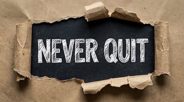 The words never quit written on a black background revealed through a torn brown paper hole