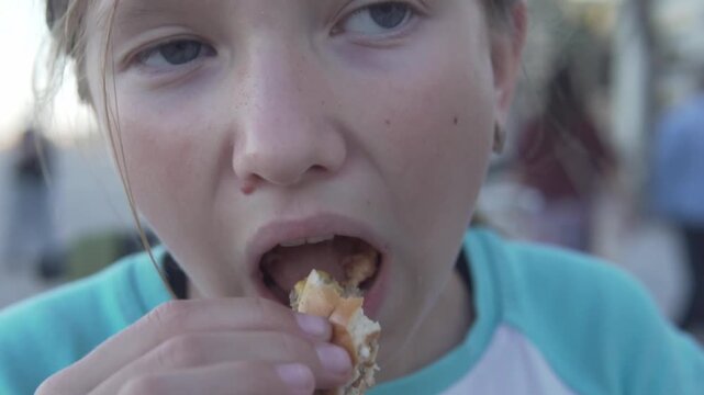 Hungry girl eating a burger outdoors, close-up of a child enjoying fast food