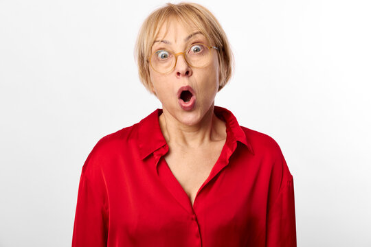 Woman wearing glasses in a red shirt, surprised with open mouth and wide eyes. Studio shot on white background. Expression of astonishment, shock, surprise, emotion.