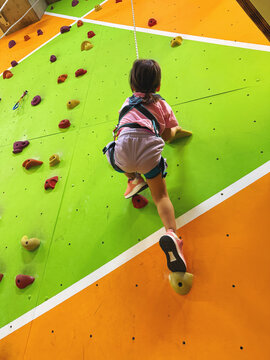Child climbing colorful indoor rock wall with safety harness, active recreation, climbing gym, physical development, adventure sport, coordination training, confidence building, healthy childhood, 