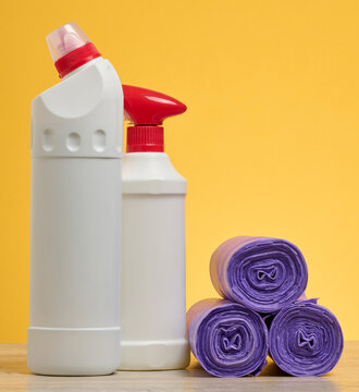 White plastic bottles of household chemicals with red lids and rolls of purple garbage bags on a yellow background