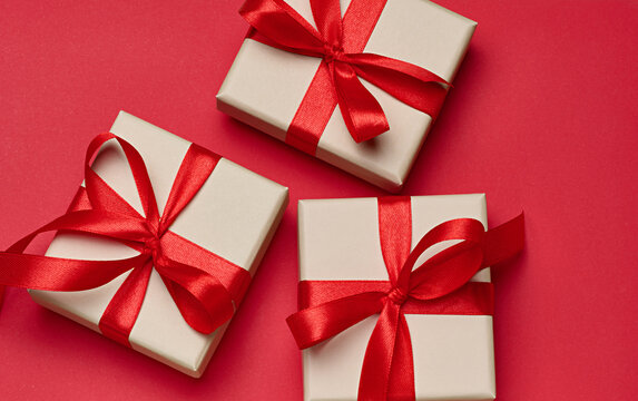 Gift boxes in beige packaging with red satin bows on a bright red background