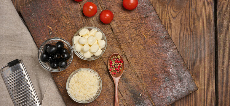 Pizza ingredients with mozzarella, grated cheese, cherry tomatoes, olives, spices in a spoon and grater