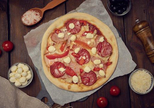 Pizza with salami, ham and mozzarella cheese on a wooden table