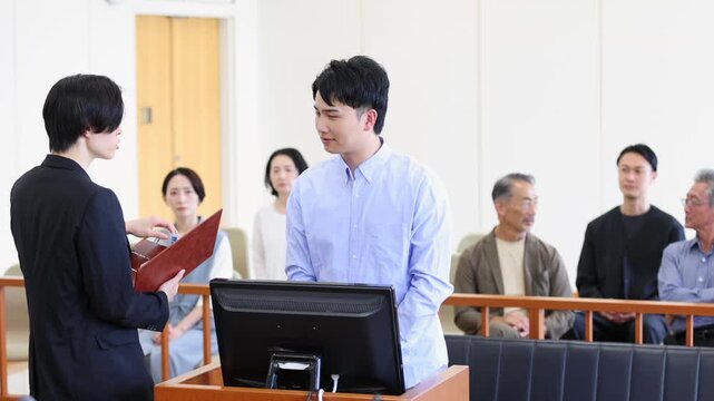法廷で証言を行う若い男性と裁判を見守る傍聴人