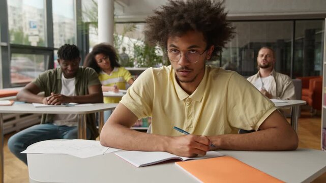 African American student guy writing test lesson suffering with bullying by rude students throwing crumpled papers balls man tired with bully problem write at lesson suffer with racism discrimination