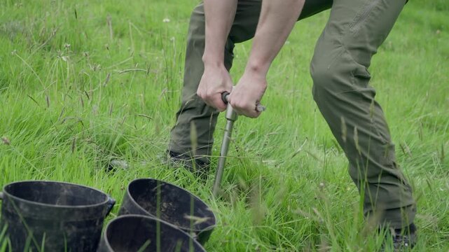 Soil scientist using a hand auger to extract a cylindrical core sample from a grassy field