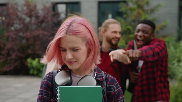 Stressed upset Caucasian girl student suffering social pressure bullied by multiracial students aggressive abuse laughing showing thumb down teasing bully in university college high school in city