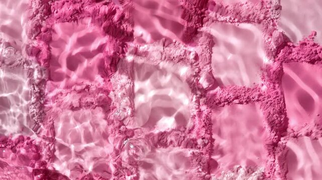 Top view extreme close-up slow motion shot of a water stream splashing over numerous pink and rose colored powder smears arranged in a mosaic pattern