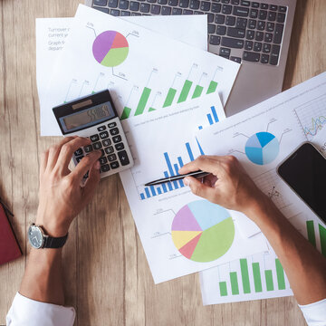 Person analyzes financial charts with calculator and pen. Hands focus on colorful pie and bar graphs. Scene suggests budgeting, finance, or business strategy. Ideal for presentations, reports
