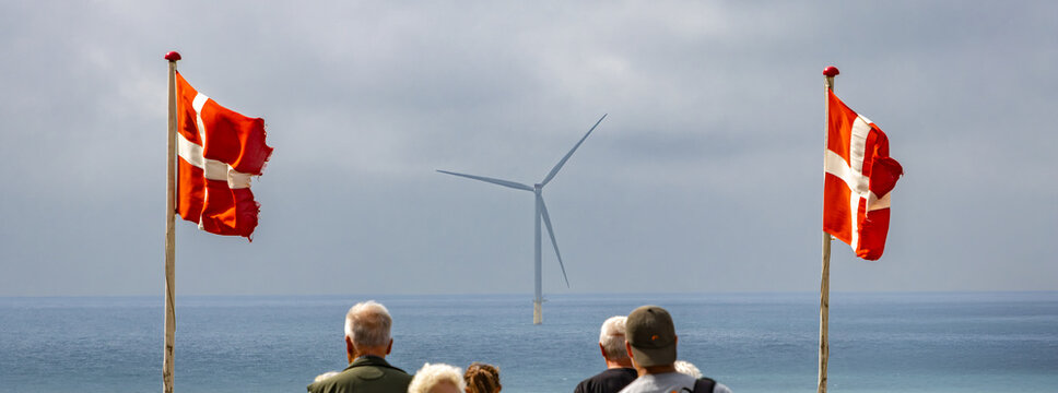 Danish flags and wind turbine by the sea, people watching