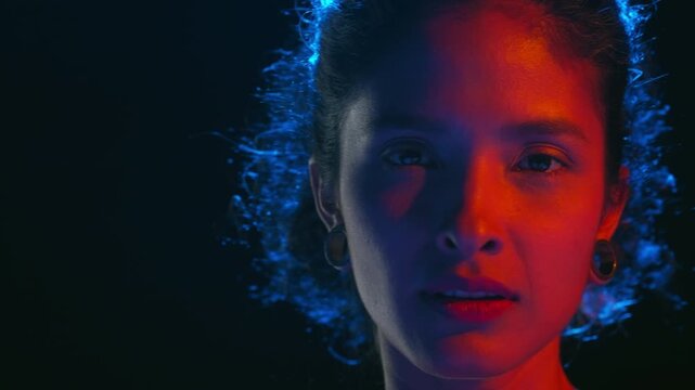 Big closeup shot of light brown skinned woman lit with red and blue lighting turn her body stroking her skin with hand from back to clavicles isolated on black | Abstract fashion concept