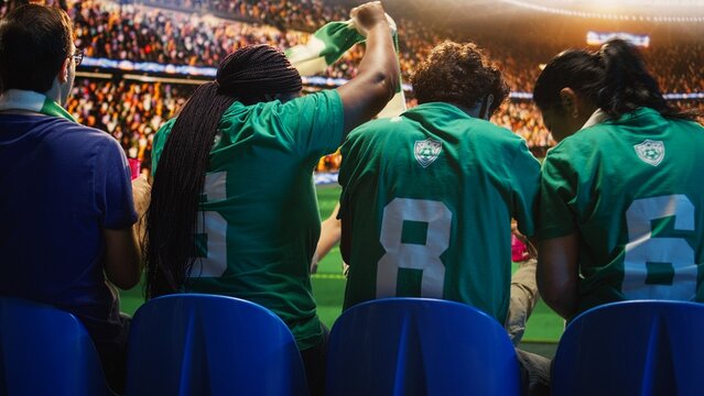 Happy soccer fans cheer players from packed stadium seats and react positively to the match, celebrating together as football supporters create lively team energy during game day.