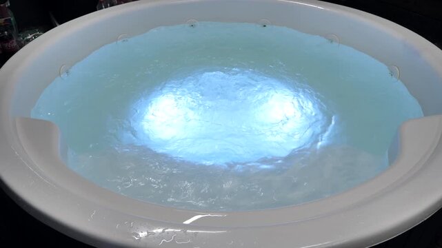 Round hot tub jacuzzi with bubbling blue water and internal illumination at night.
