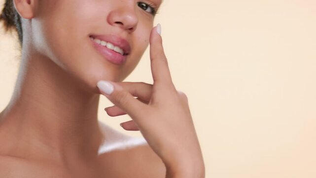 Tight shot of beauty skincare model touches her jawline and face skin with hand dorsal showing her balanced skin on tan backdrop | Facial serum commercial footage