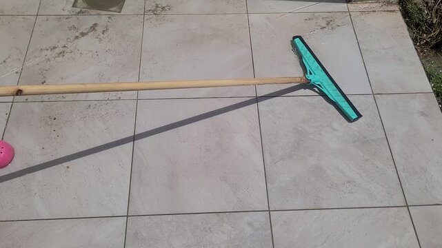 Person cleaning tile floor with squeegee on patio