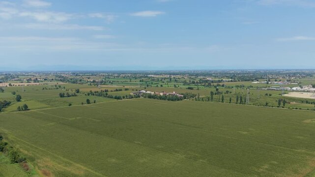 Vast Farmland Under Blue Sky: An expansive aerial view showcases a patchwork of lush green agricultural fields stretching towards the horizon under a clear, Tavazzano con Villavesco, Lodi, Italy