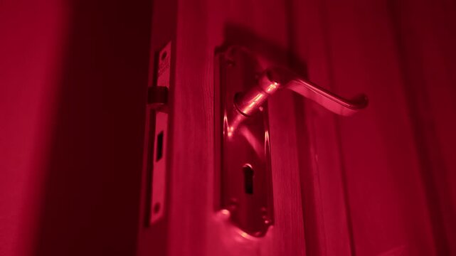 Close up metal door handle on wooden door with dramatic red lighting and shallow focus