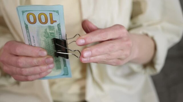 Woman's hands clipping a stack of one hundred dollar bills. Female hands holding a large wad of one hundred dollar bills, using a black binder clip to secure the cash stack, symbolizing wealth