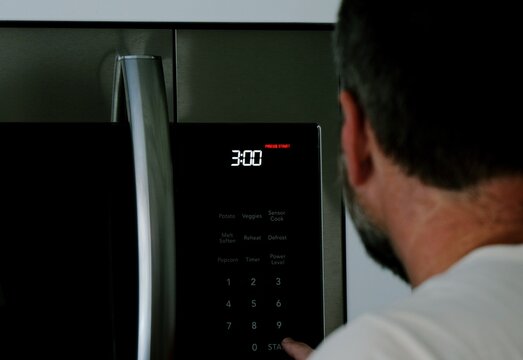 Man setting digital clock time on kitchen microwave stove appliances, representing changing clocks - daylight savings time, spring forward, fall back