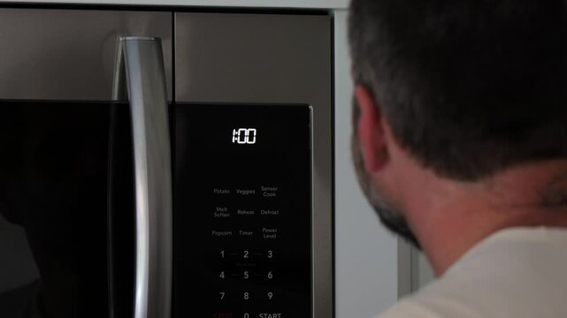 Man setting digital clock time on kitchen microwave stove appliances, representing changing clocks - daylight savings time, spring forward, fall back