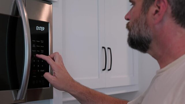 Man setting digital clock time on kitchen microwave stove appliances, representing changing clocks - daylight savings time, spring forward, fall back