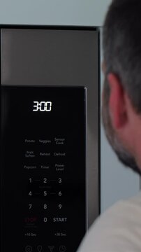Man setting digital clock time on kitchen microwave stove appliances, representing changing clocks - daylight savings time, spring forward, fall back