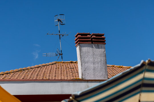 Traditional concrete chimney and tv antenna on ceramic tile house roof against clear blue sky during sunny summer day in coastal town in Italy.