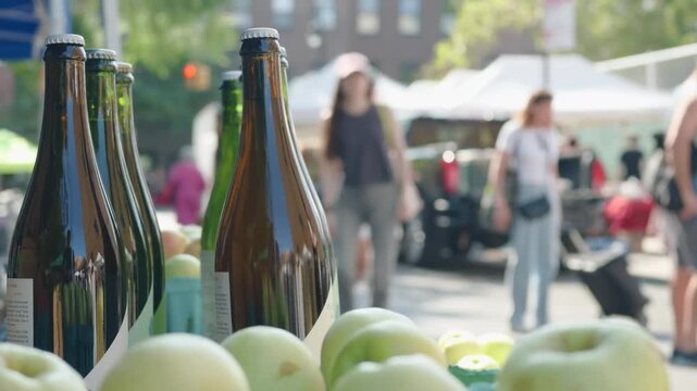 people walk past bottles of apple cider for sale at Brooklyn farmers market