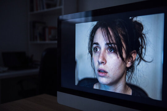 Shocked person's face reflected on computer screen showing hyperrealistic deepfake AI deception