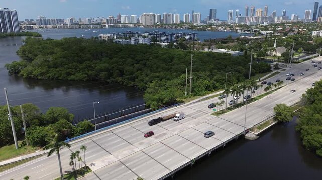 Aerial drone view of a multilane highway with traffic crossing a mangrove estuary near a coastal city skyline, Florida