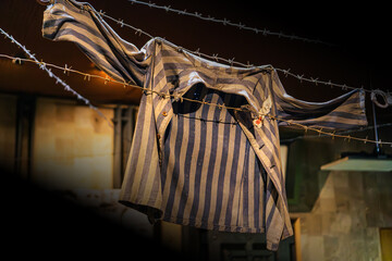 Worn prison uniform hanging on barbed wire fence, fastened with buttons, showing signs of wear and tear, against dimly lit blurred background of prison architecture, creating somber atmosphere with © Mister