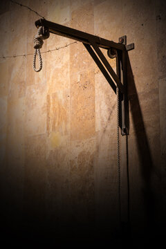 Historical noose and metal frame on aged wall, evocative somber composition, light beige textured backdrop, muted color scheme, dramatic lighting contrast, rustic materials, shadow depth, reflection