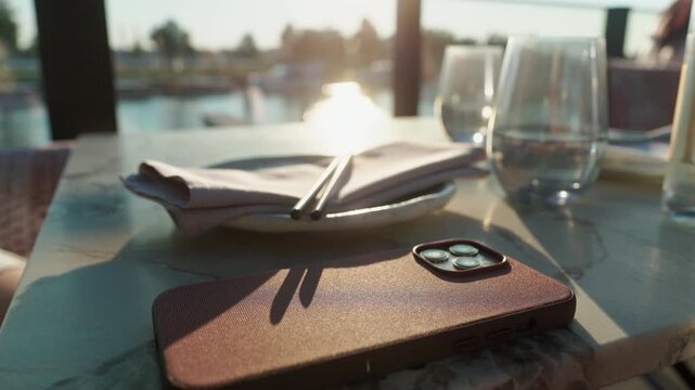 Smartphone on restaurant table with napkin, chopsticks, and glassware in warm sunset light