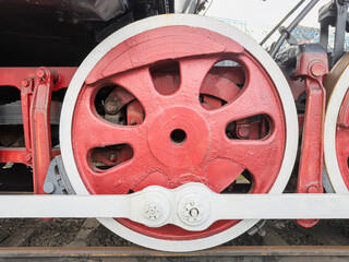 Steam locomotive wheel close-up, intricate metal construction, bold red with white accents, worn paint, industrial heritage, railway yard setting, natural daylight lighting, textured background © Mister