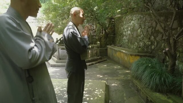 Two Buddhist monks in traditional robes bowing and praying together in a tranquil temple garden