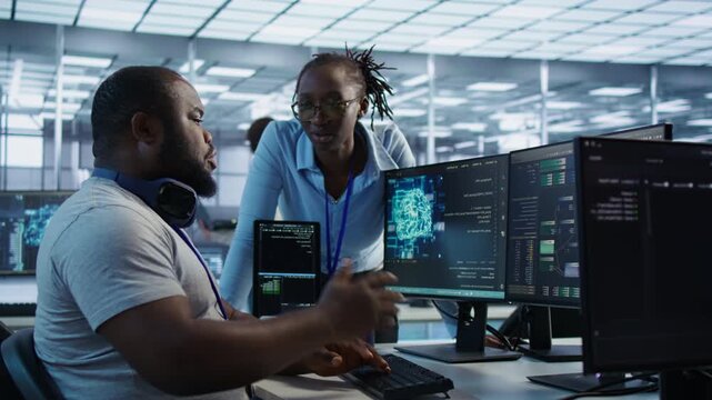 IT specialist talks with a coworker while monitoring AI supercomputers from an alternate angle, connecting teamwork with technical infrastructure oversight.