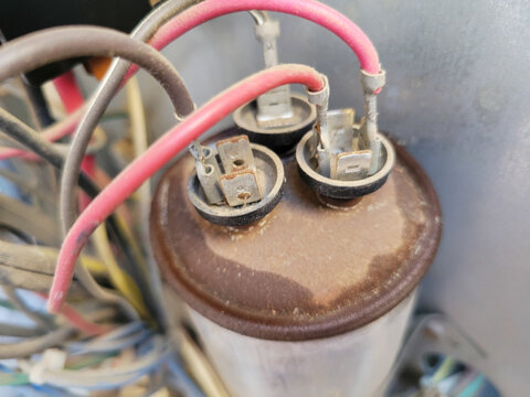 Top view of a rusty and dusty and leaking dual run capacitor showing spade terminals and connected wires in an outdoor air conditioner